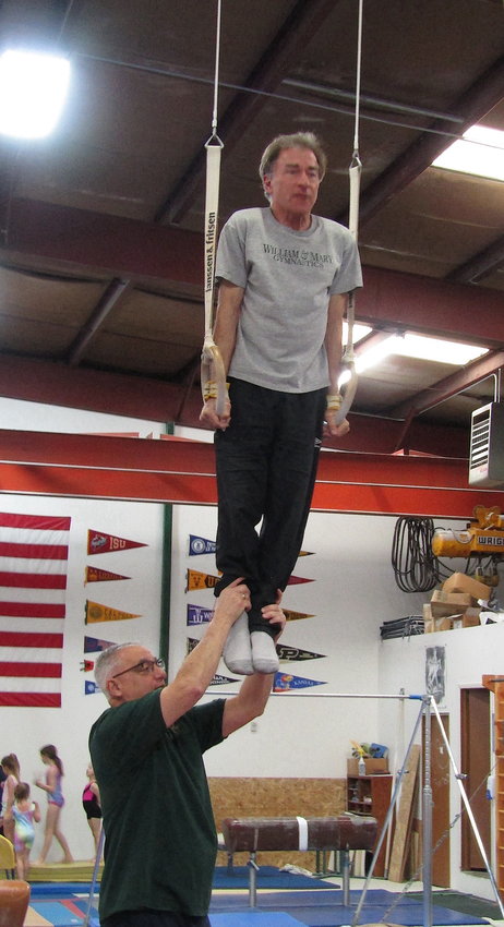Steve Artemis, owner of Golden Gymnastics, steadies Monty Estis on the rings before Estis performs a planche. Estis, a member of the Evergreen Park & Receation District board, was looking for a goal as he trained in gymnastics.